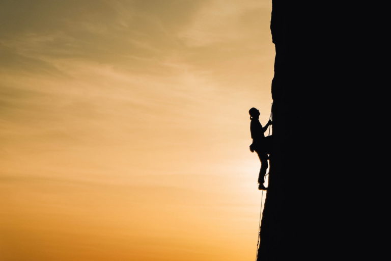 Silhouette of person climbing a mountain with orange sky